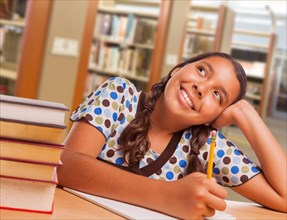 Happy hispanic girl student with pencil and books daydreaming while studying in library
