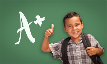 Cute hispanic boy with thumbs up in front of A+ written on chalk board