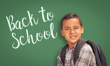 Cute hispanic boy wearing A backpack in front of chalk board with back to school written on it