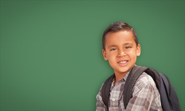Cute hispanic boy with backpack in front of blank chalk board