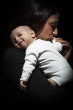 Young attractive ethnic woman kisses her newborn baby hand under dramatic lighting