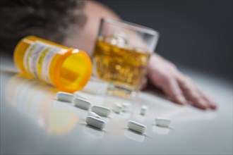 Unconscious man face down behind scattered prescription drugs and glass of alcohol
