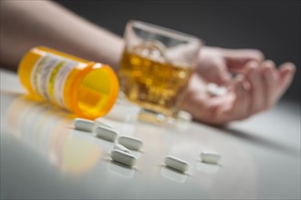 Hand laying on ground behind scattered prescription drugs and glass of alcohol