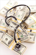 Question mark shaped stethoscope laying on stacks of hundred dollar bills with narrow depth of field