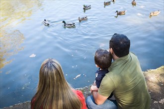 mixed-race mother and father with son at the park duck pond