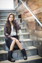 Portrait of a pretty mixed-race young adult woman sitting on a staircase wearing leather boots and jacket