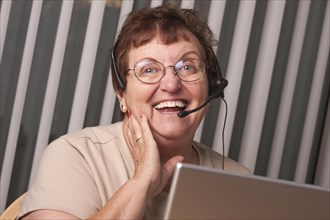 Smiling senior adult woman with telephone headset in front of computer monitor