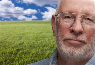 Melancholy senior man with grass field behind him