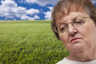 Melancholy senior woman with grass field behind her