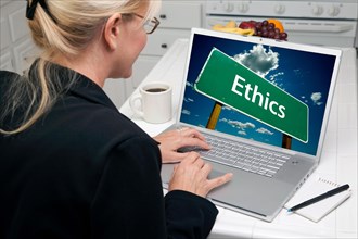 Woman in kitchen using laptop with ethics road sign on screen. screen can be easily used for your own message or picture. picture on screen is my copyright as well