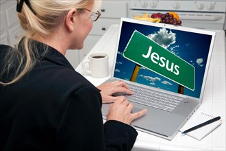 Woman in kitchen using laptop with jesus road sign on screen. screen can be easily used for your own message or picture. picture on screen is my copyright as well