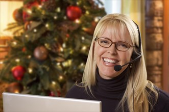 Happy woman with phone headset in front of christmas tree and computer screen