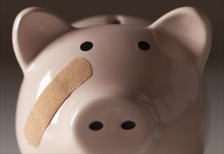 Piggy bank with bandage on face on gradated background