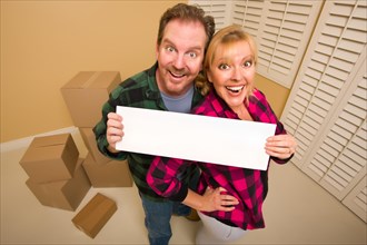 Happy goofy couple holding blank sign in room with packed boxes