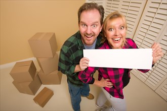 Happy goofy couple holding blank sign in room with packed boxes