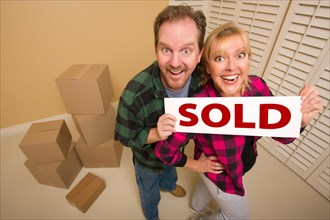 Goofy couple holding sold sign in room surrounded by cardboard boxes