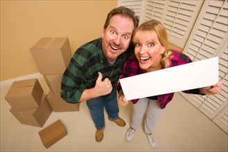 Goofy thumbs up couple holding blank sign in room with packed cardboard boxes