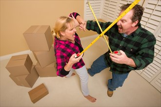 Couple having a fun sword fight with their tape measures surrounded by packed moving boxes