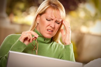 Grimacing woman with glasses using laptop suffering a painful headache