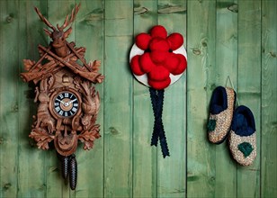 Black Forest cuckoo clock with Bollen hat and straw shoes in front of green wooden wall