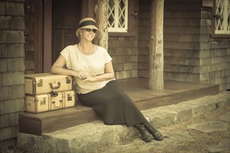Pretty 1920s dressed girl next to suitcases on porch with vintage effect added