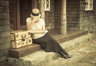 Distressed 1920s dressed girl next to suitcases on porch with vintage effect added