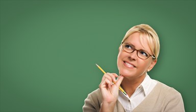 Attractive young woman with pencil and glasses in front of blank chalk board