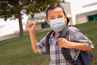 Hispanic student boy wearing face mask with backpack on school campus