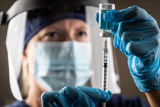 Doctor or nurse wearing surgical gloves holding vaccine vial and medical syringe