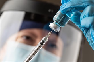 Doctor or nurse wearing surgical gloves holding vaccine vial and medical syringe