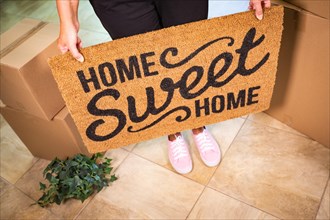 Woman in pink shoes holding home sweet home welcome mat