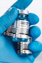 Doctor or nurse wearing surgical glove holding coronavirus COVID-19 vaccine vials