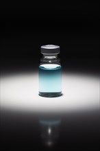 Medicine vial with light blue chemical spot lit on reflective background
