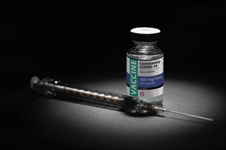 Syringe needle and coronavirus COVID-19 vaccine vial spot lit on dark background