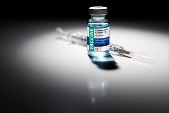 Coronavirus COVID-19 vaccine vial and syringe spot lit on reflective surface