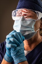 American flag reflecting on distressed praying female medical worker wearing protective face mask and goggles