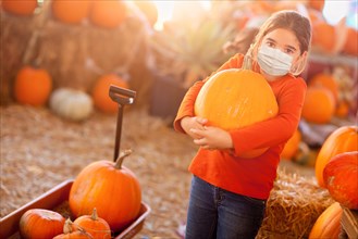 Cute girl choosing A pumpkin at pumpkin patch wearing medical face mask