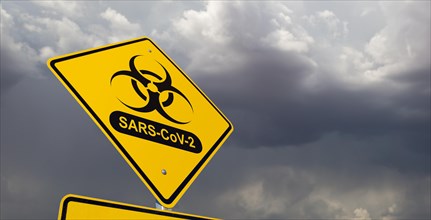 Bio-hazard symbol with sars-cov-2 coronaravirus yellow road sign against ominous stormy cloudy sky