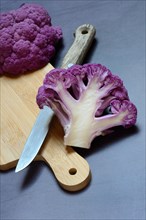Halved purple cauliflower on wooden board with kitchen knife