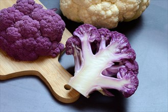Halved purple cauliflower on wooden board with kitchen knife