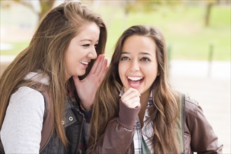 Two attractive mixed-race woman with backpacks whispering secrets outside