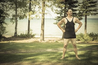 Goofy gentleman dressed in 1920's era swimsuit holding suitcases on porch of cabin