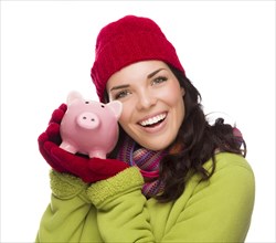 Happy smiling mixed-race woman wearing winter clothing holding piggybank isolated on white background