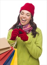 mixed-race woman wearing winter clothing holding shopping bags texting on cell phone isolated on white background