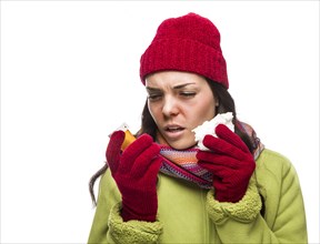 Sick mixed-race woman wearing winter hat and gloves blowing her sore nose and holding empty medicine bottle isolated on white