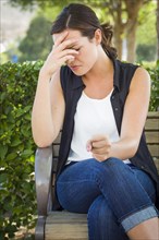 Upset young woman sitting alone on bench outside with her head in her hand and clenched fist