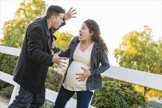 Stunned and excited pregnant woman and husband with hand on belly outside