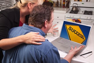 Couple in kitchen using laptop with yellow success road sign on the screen