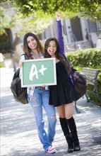 Excited mixed race female students holding chalkboard with A+ written on it