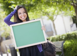 Portrait of an attractive excited mixed race female student holding blank chalkboard and carrying backpack on school campus